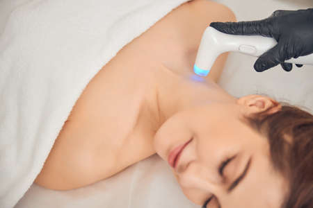 Young brunette woman relaxing while getting procedure at beauty center with help of special electric deviceの写真素材