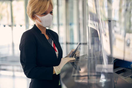 Elegant businesswoman in protective face mask and sterile gloves holding smartphone and airplane ticketの写真素材