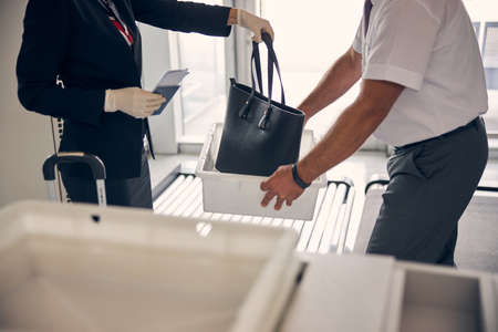 Close up of female traveler putting elegant handbag in white box while airport worker holding...