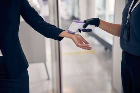 Close up of female airport security guard measuring lady temperature with digital medical thermometerの写真素材