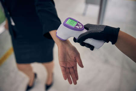 Close up of airport security guard measuring lady temperature with digital medical thermometer during pandemicの写真素材