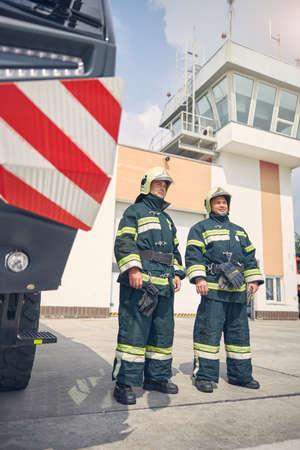 Full length portrait of two males standing near the fire modern machine in the outdoors