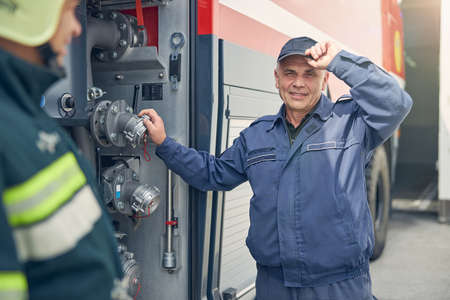 Close up portrait of smiling driver of fire truck standing near it while putting hand on faucet of waterの写真素材