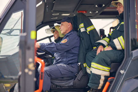 Side view of professional men in the fire engine dressed the protective uniform with helmet on headの写真素材