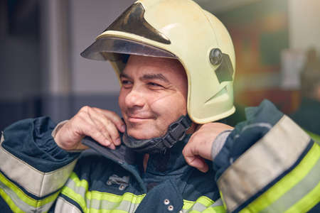 Waist up portrait of confident firefighter posing at the photo camera while holding uniformの写真素材