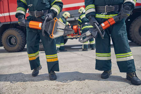 Cropped head of two strong firefighters holding an expansion device in hands