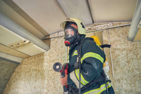 Man holding water hose in hands while standing at the indoors in yellow helmet
