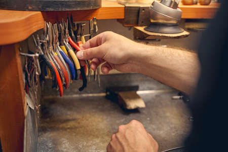 Cropped photo of an experienced jewelry maker choosing a pair of pliers for his work