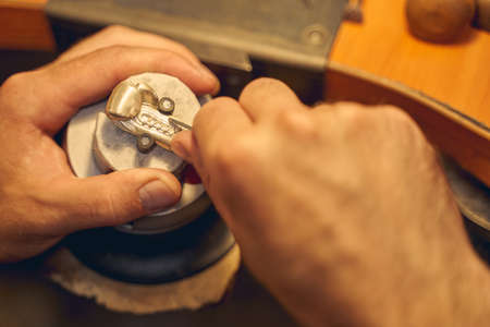 Close up of Caucasian male hands treating a metal pendant in an engraving block ball vise