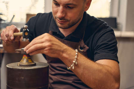 Front view of a young metalsmith treating a metal part on a double horn anvil