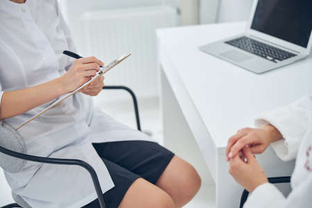 Cropped head of female doctor or nurse writing medical report to clipboard at hospital