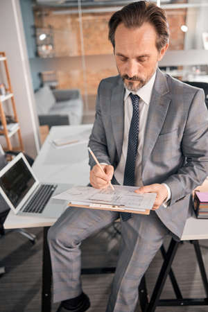 Bearded gentleman in stylish suit sitting on office table and working on new business project