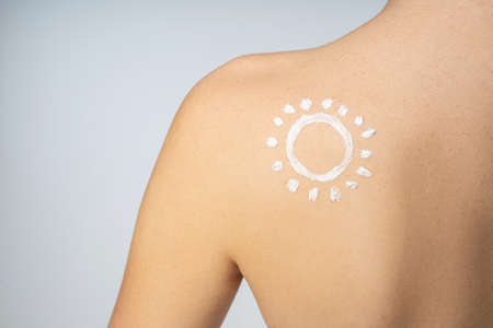 Close up of female shoulder with sun protection cream in the shape of sun on her skinの写真素材