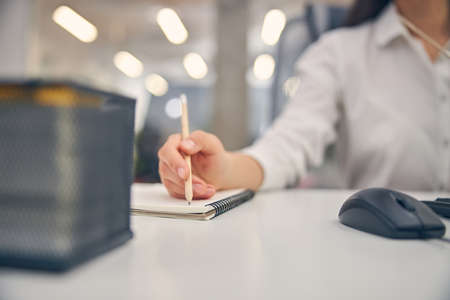 Young brunette woman sitting at the table in front of her computer while writing notices during...