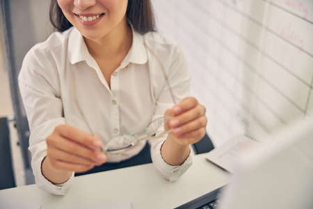 Pleased female person keeping smile on her face while holding glasses in both handsの写真素材