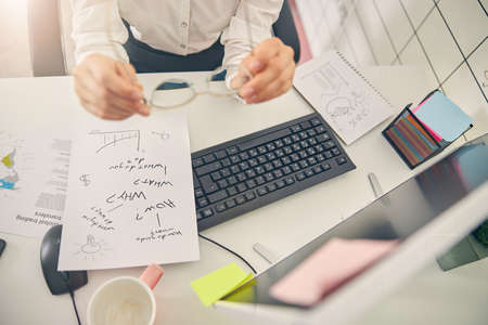 Young female person sitting at her workplace while making notes during online conference