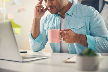 Kind young man sitting at the table and enjoying his coffee during break