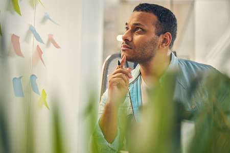 Kind young male person turning his head while looking at his notes on the wall