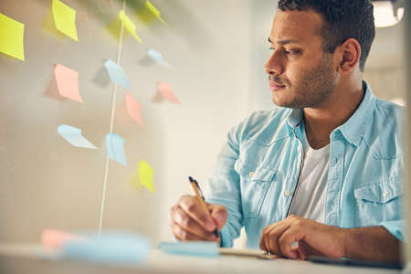Close up of kind male person sitting at his workplace while making notes for project presentation