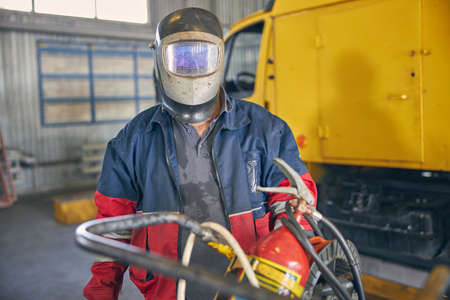 Busy welder wearing mask before working with dangerous instrument, holding fire extinguisher