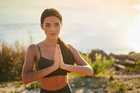 Beautiful sporty lady in crop top keeping hands in prayer position while doing meditation yoga exercise outdoorsの写真素材