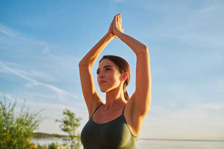 Attractive lady looking away and smiling while doing yoga exercise under beautiful blue skyの写真素材