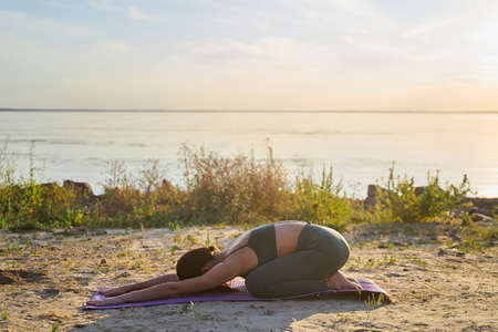 Sporty fit lady in leggings and crop top practicing yoga on the beach early in the morningの写真素材