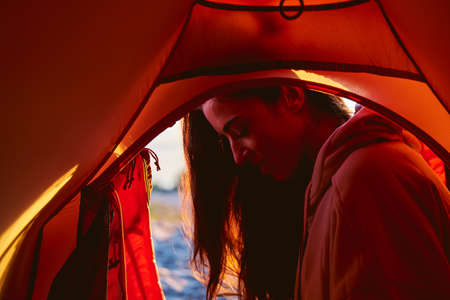 Attractive female traveler looking down and smiling while resting near touristic tent