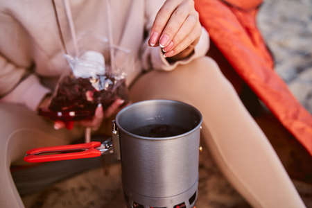 Close up of young woman adding ingredient to herbal tea while sitting in camp tentの写真素材