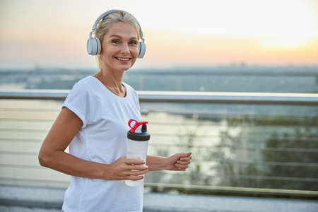 Waist-up portrait of a high-spirited fit pretty lady in wireless headphones posing for the camera
