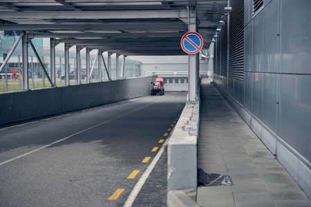 Tunnel with tractor for luggage transportation, gray building, asphalt road and warning sign