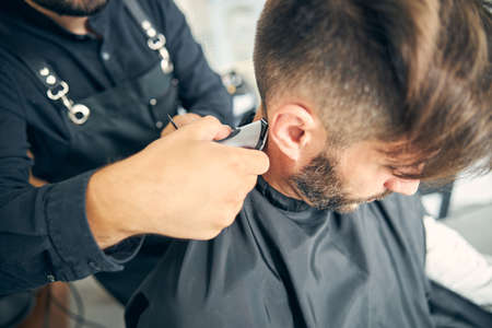 Focused photo on young man being covered with cape while doing haircuttingの写真素材