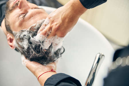Frustrated man leaning on sink while enjoying hair care procedureの写真素材