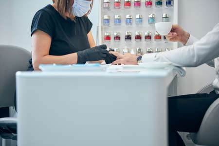 Busy young man sitting in front of his master while doing manicure before business meeting