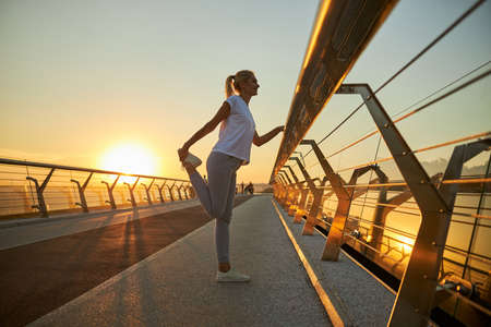 Beautiful smiling lady in sportswear doing exercise early in the morning on the streetの写真素材