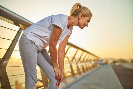 Beautiful sporty woman in white shirt suffering from knee pain after morning training