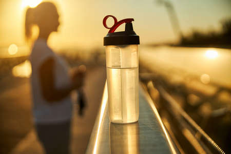 Close up of plastic sport bottle of refreshing drink and sportswoman on backgroundの写真素材
