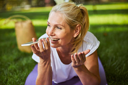 Beautiful joyful lady using speakerphone while talking on mobile phone outdoors