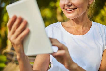 Close up of joyful lady holding white electronic pad PC and smiling while spending time outdoorsの写真素材