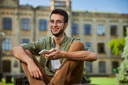 Handsome cheerful university student with a smartphone in his hand looking in front of himの写真素材