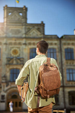 Back view of a Caucasian male student with dark hair approaching an old university buildingの写真素材