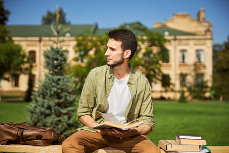 Front view of a young man with an open textbook in his hand looking away