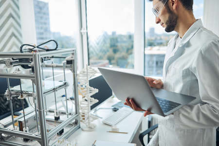 Side view of a serious male scientist staring at a device printing a three-dimensional object
