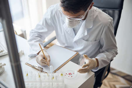Dark-haired Caucasian young man in a protective mask and sterile gloves analyzing the blood sample