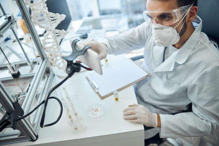 Serious bearded young man in a face mask and latex gloves sitting at a tableの写真素材