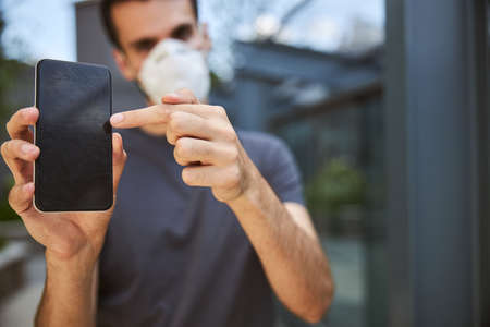 Cropped photo of a young Caucasian man pointing at his gadget with an index finger