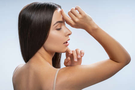 Back view of a relaxed young female with loose long dark hair touching her forehead and chin with handsの写真素材