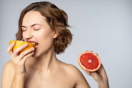 Close up portrait of a dark-haired young Caucasian woman biting a bitter grapefruit with closed eyesの写真素材