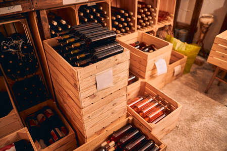 Wine cellar with glass bottles of alcoholic drink in wooden boxes and wine racks with vintage year...