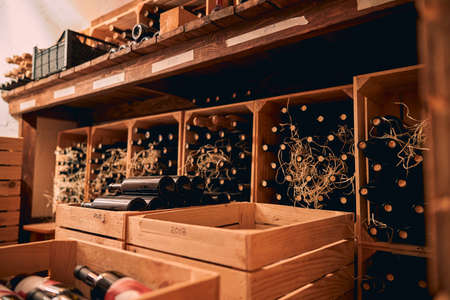 Storage room or wine cellar with bottles of alcoholic drink in wooden boxes and shelves with vintage year labelsの写真素材
